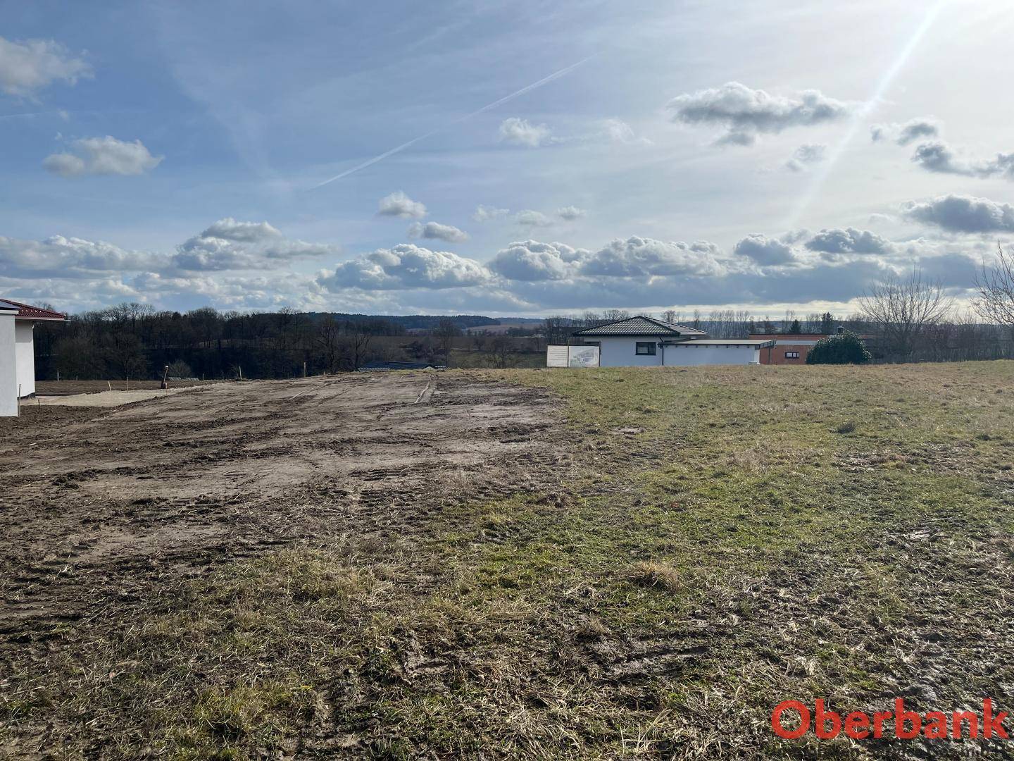 Großes, offenes Grundstück mit Gras und Erde, umgeben von vereinzelten Häusern und weiter Landschaft.