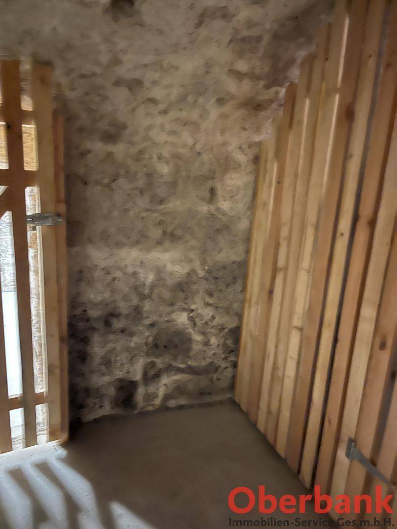 Rustikaler Kellerraum mit rauen Steinwänden und vertikalen Holzlatten an einer Seite.