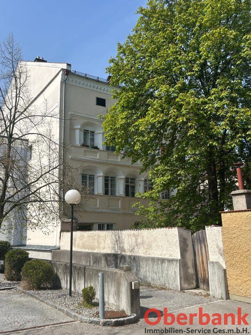 Historisches Gebäude mit klassischer Fassade, umgeben von üppiger grüner Vegetation und Bäumen.