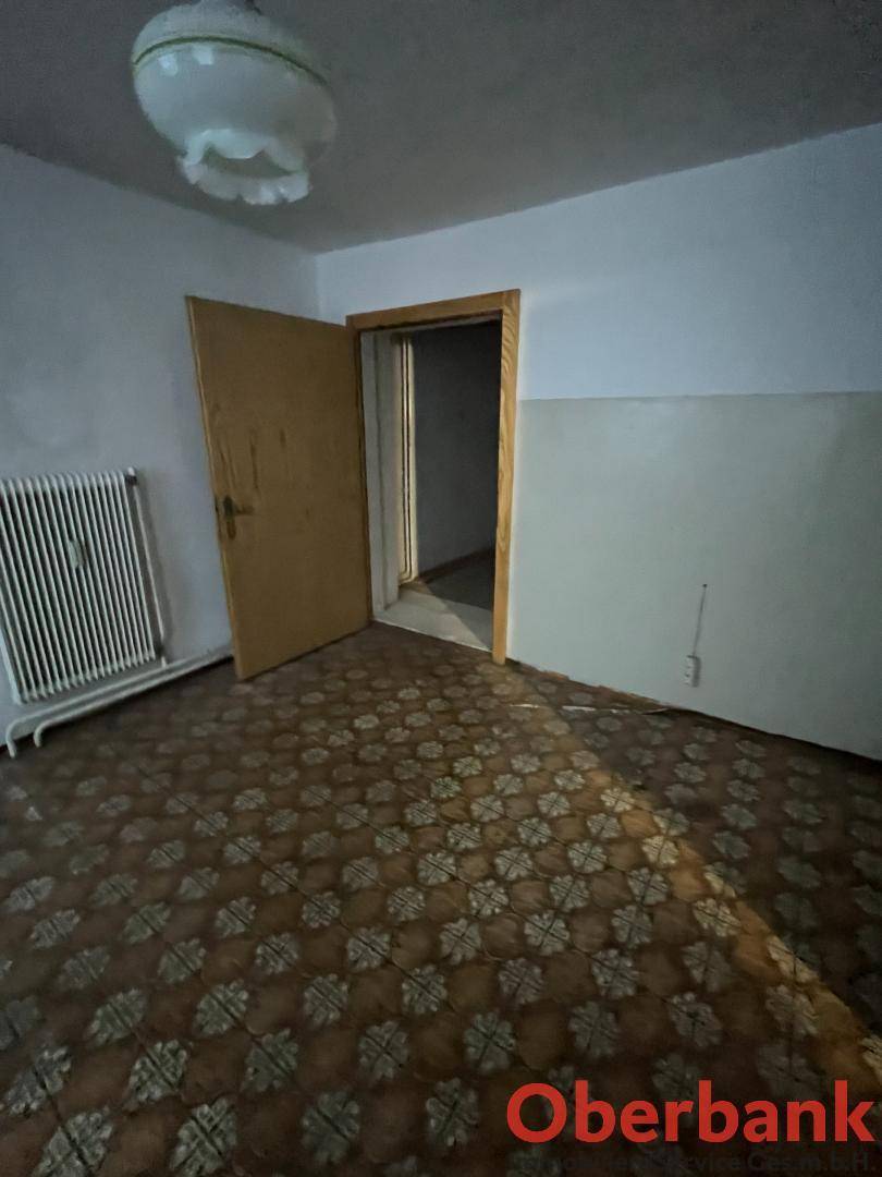 Raum mit gemustertem Bodenbelag, Heizkörper und einer Holztür, die in einen anderen Bereich führt.