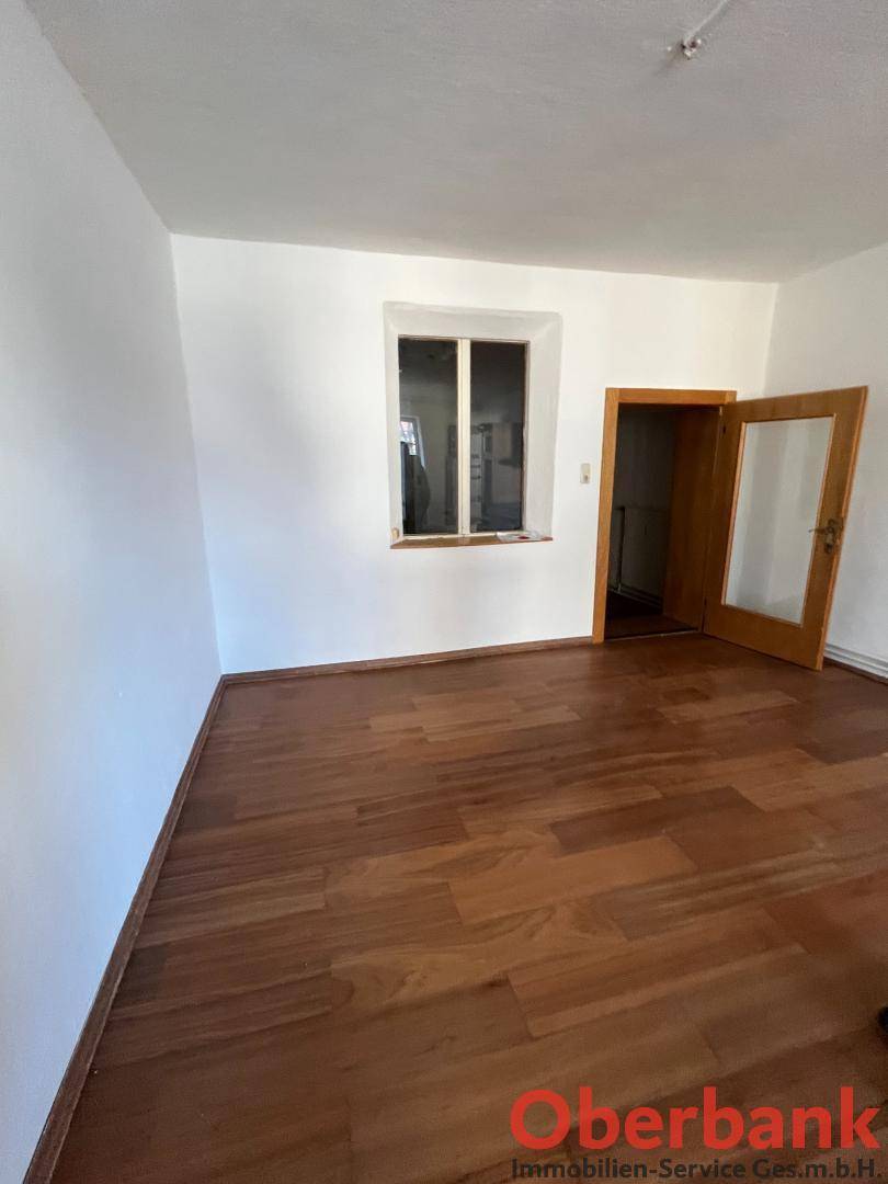 Leerer Raum mit Holzplankenboden und einem Fenster, das Tageslicht hereinlässt.