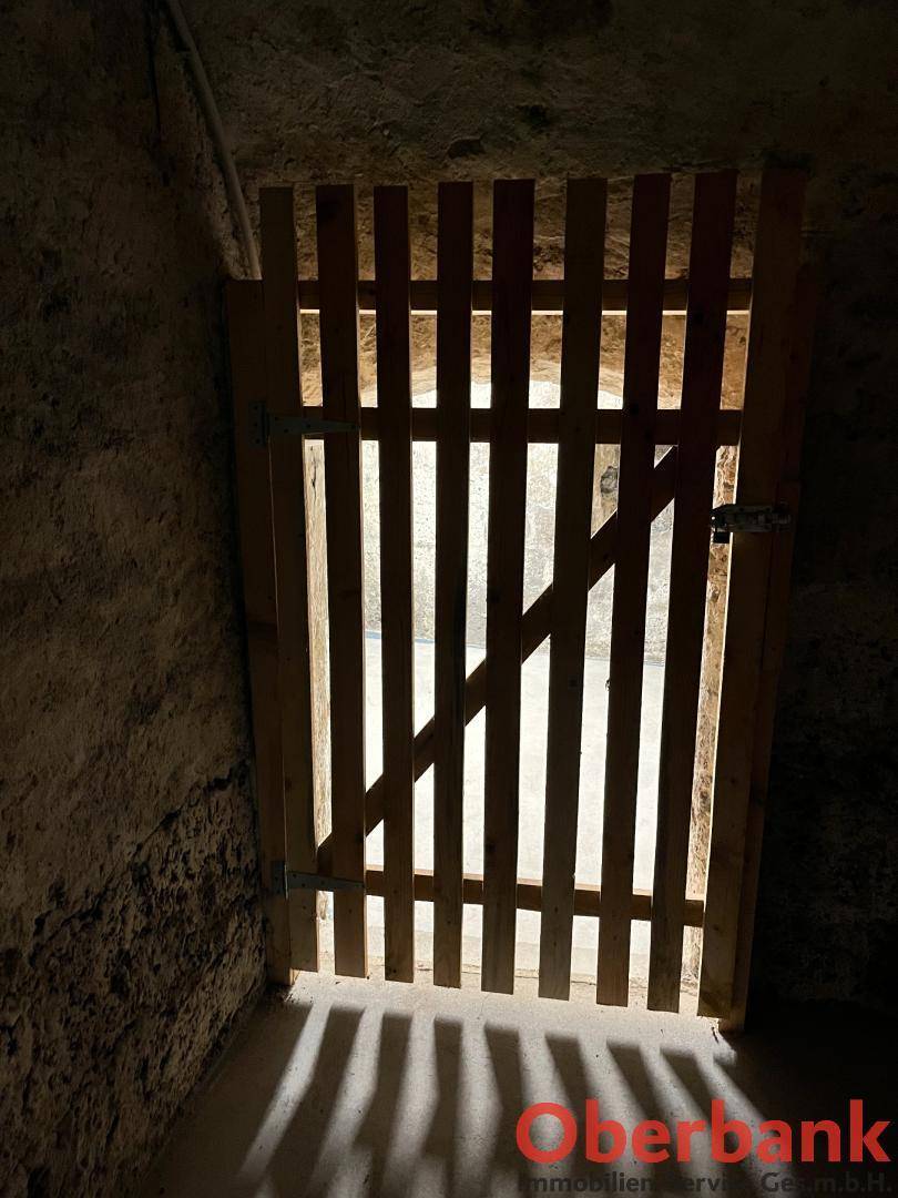 Dunkler Kellerraum mit einer einfachen Holztür, die einen Lichtschimmer hereinlässt.