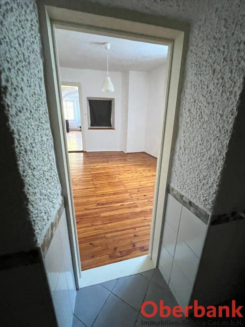 Blick durch eine Tür in einen hellen Raum mit glänzendem Holzplankenboden und weißen Wänden.