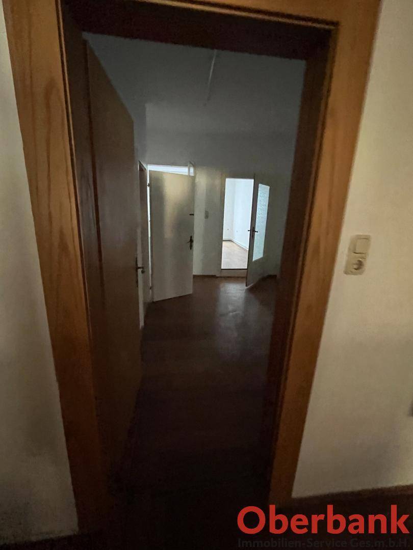 Blick durch eine Tür in einen Flur mit dunklem Bodenbelag und weiteren Türen im Hintergrund.