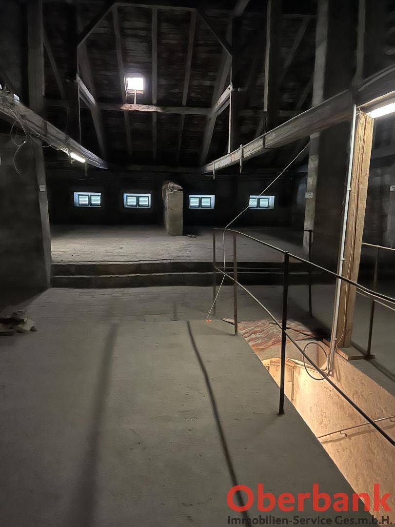 Großer, leerer Dachboden mit sichtbaren Holzbalken und kleinen Fenstern, bereit zum Ausbau.