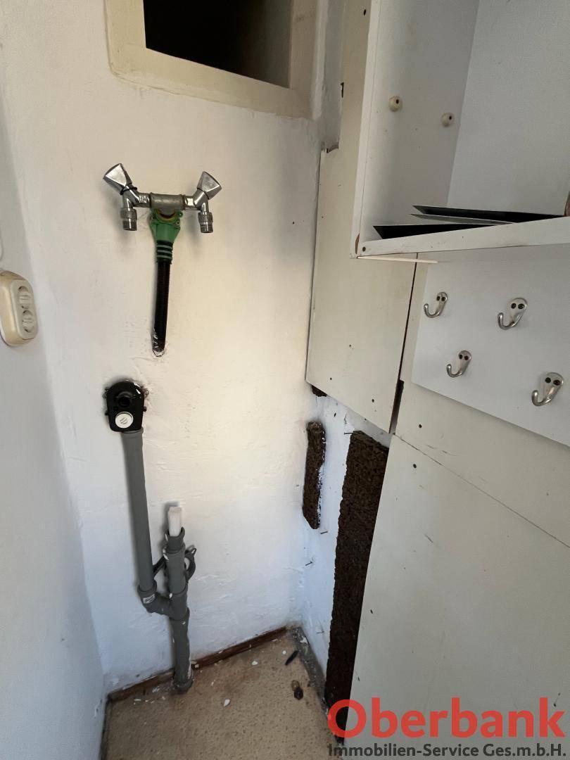 Kleiner Hauswirtschaftsraum mit sichtbaren Wasseranschlüssen und einem einfachen Wandschrank.