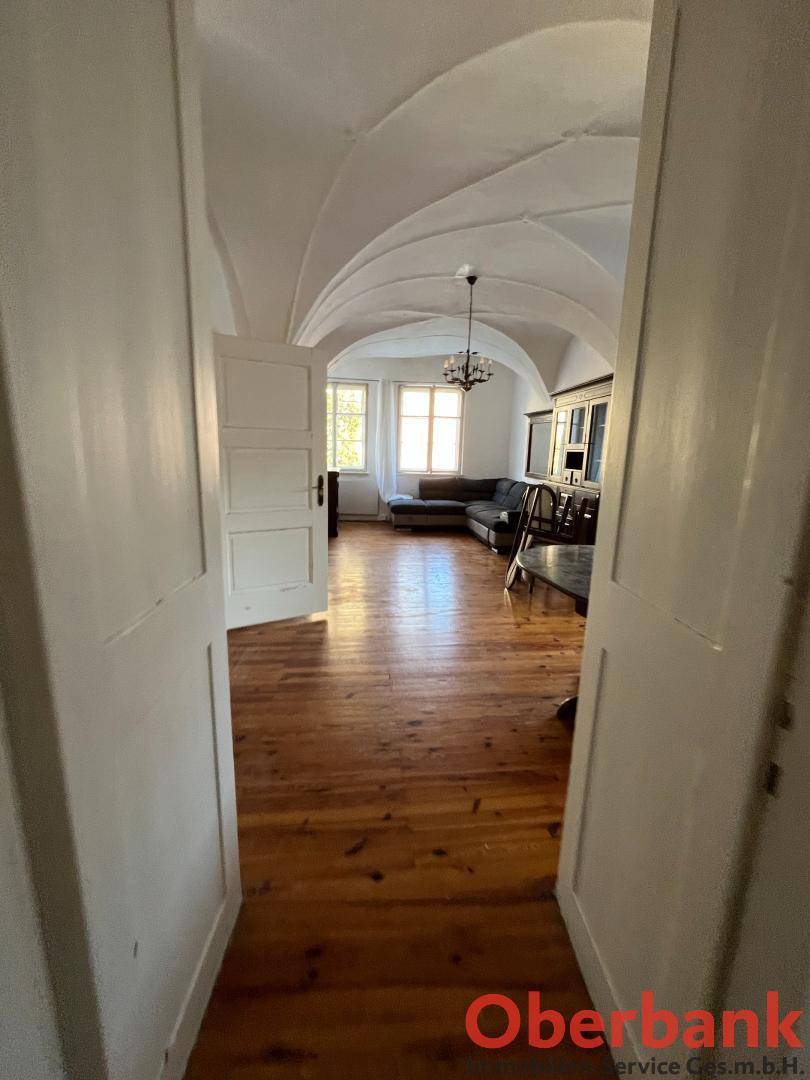 Geräumiges Wohnzimmer mit Holzboden, Gewölbedecke und einem Kronleuchter, durch eine Tür gesehen.