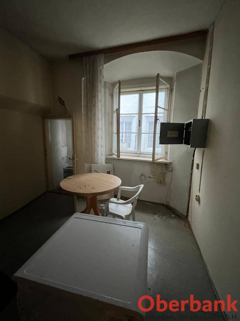 Kleiner, renovierungsbedürftiger Raum mit einem Tisch, Stuhl und einem geöffneten Fenster.