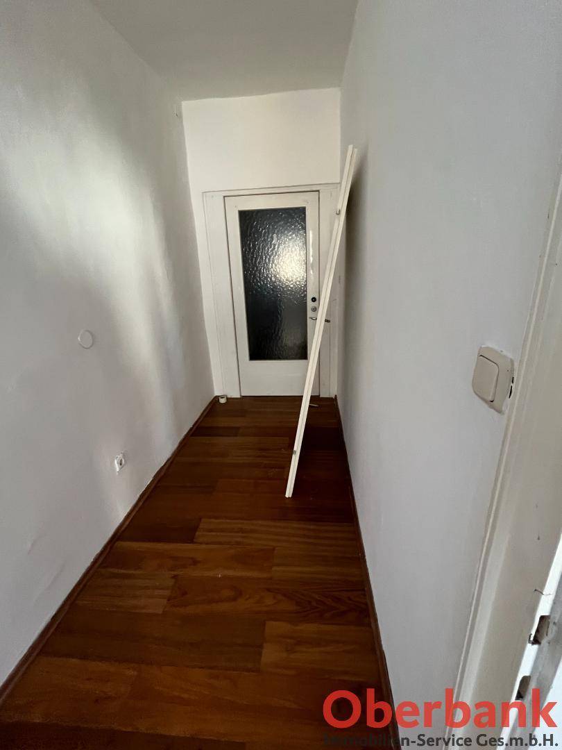 Schmaler Flur mit Holzplankenboden und einer Tür am Ende, die zu einem weiteren Raum führt.