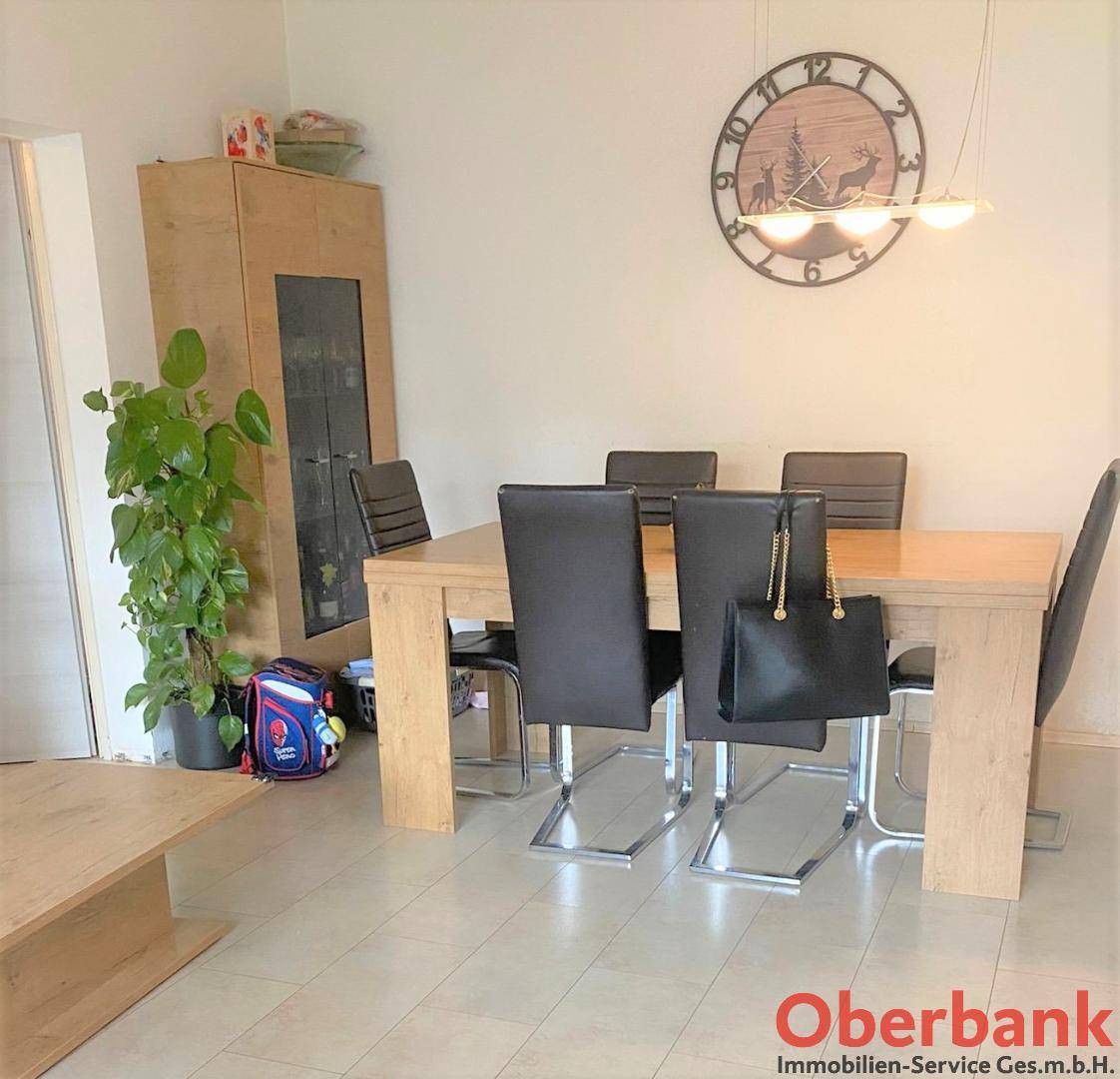 Essbereich mit hellem Holztisch und schwarzen Stühlen, ergänzt durch eine Wanduhr.
