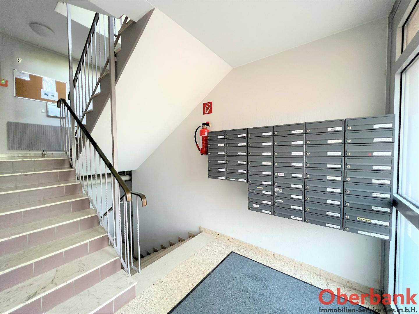 Treppenhaus im Eingangsbereich mit Briefkästen und Brandschutzvorrichtung, funktional gestaltet.