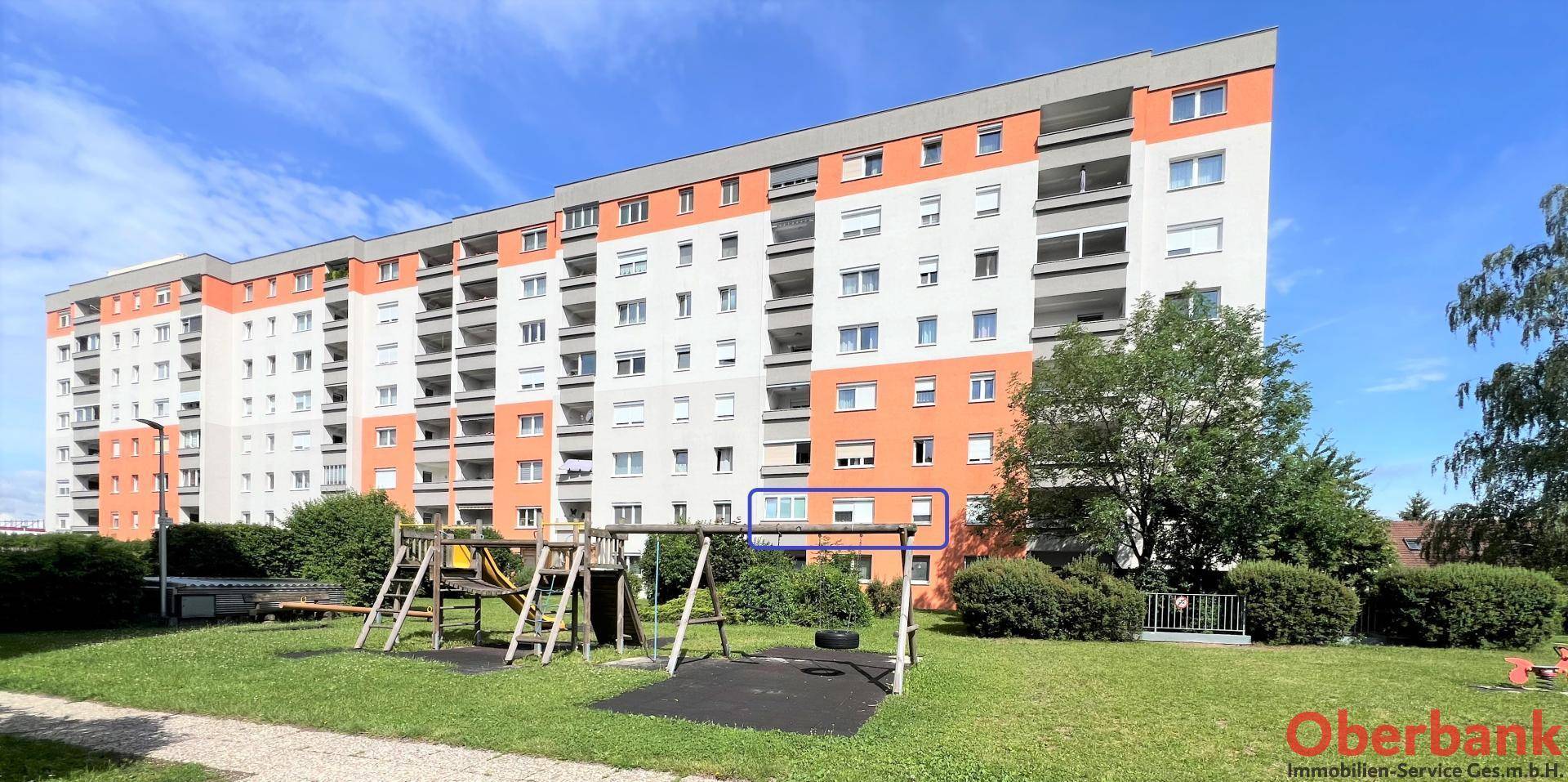 Großes Mehrfamilienhaus mit orangefarbenen Akzenten und einem Spielplatz im Vordergrund.