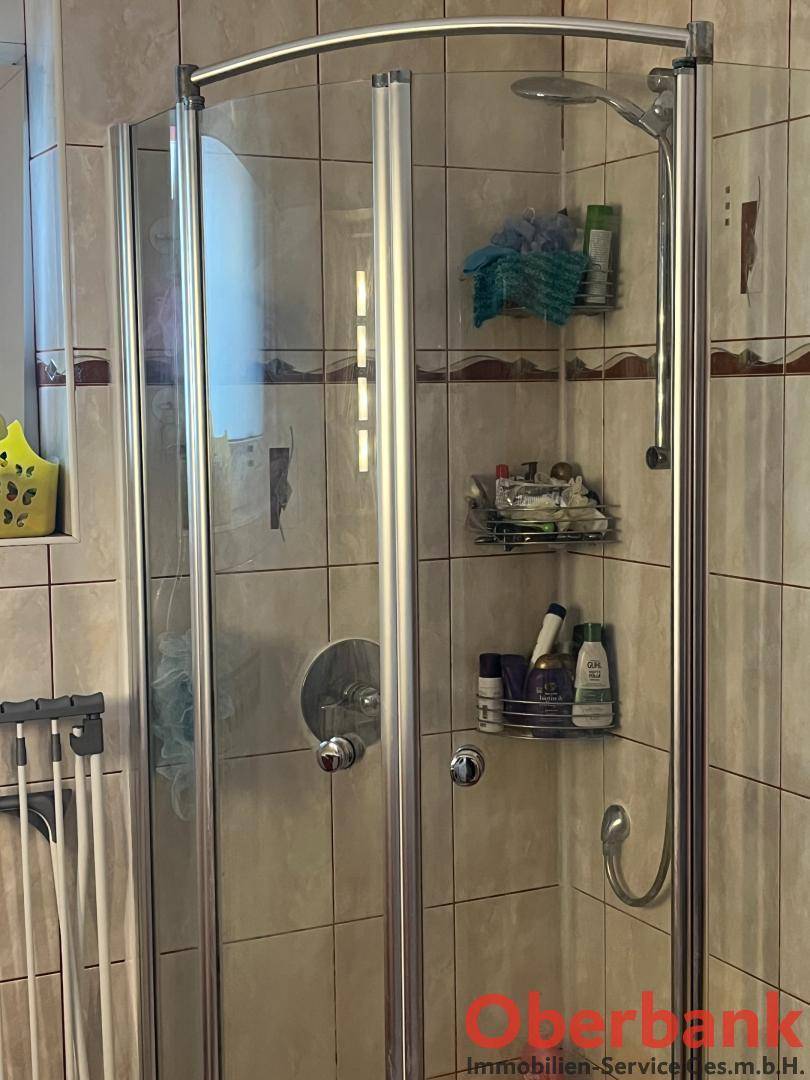 Badezimmer mit Duschkabine, hellen Fliesen und praktischen Ablagen.