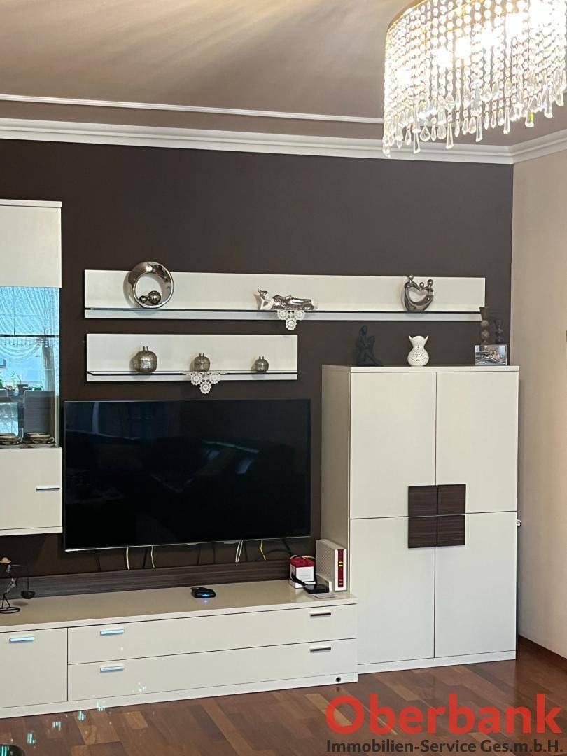 Wohnzimmer mit moderner TV-Wand, Vitrinen und einem eleganten Kronleuchter.