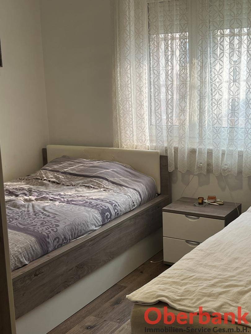 Helles Schlafzimmer mit Einzelbetten, Holzboden und Fenster mit Vorhängen.