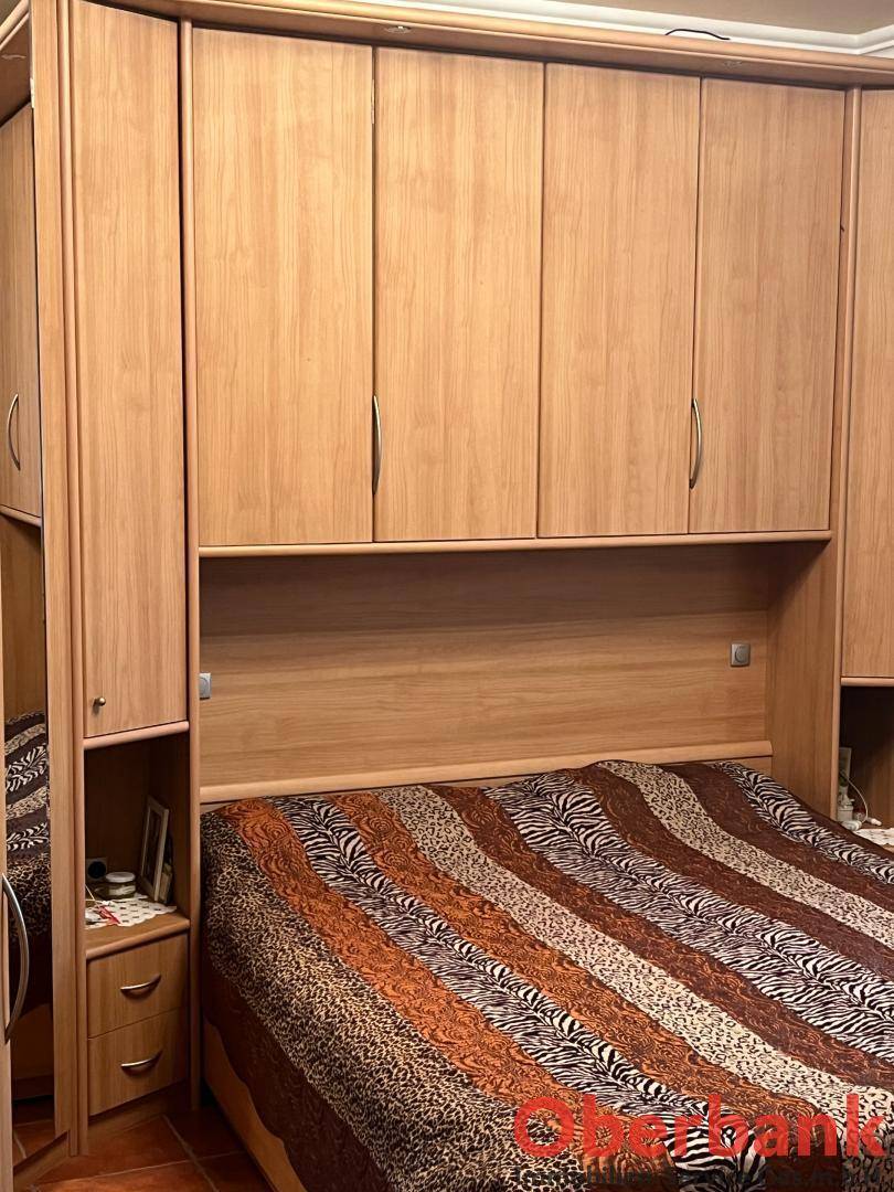 Schlafzimmer mit großem Bett, integrierten Holzschränken und gemustertem Bettzeug.