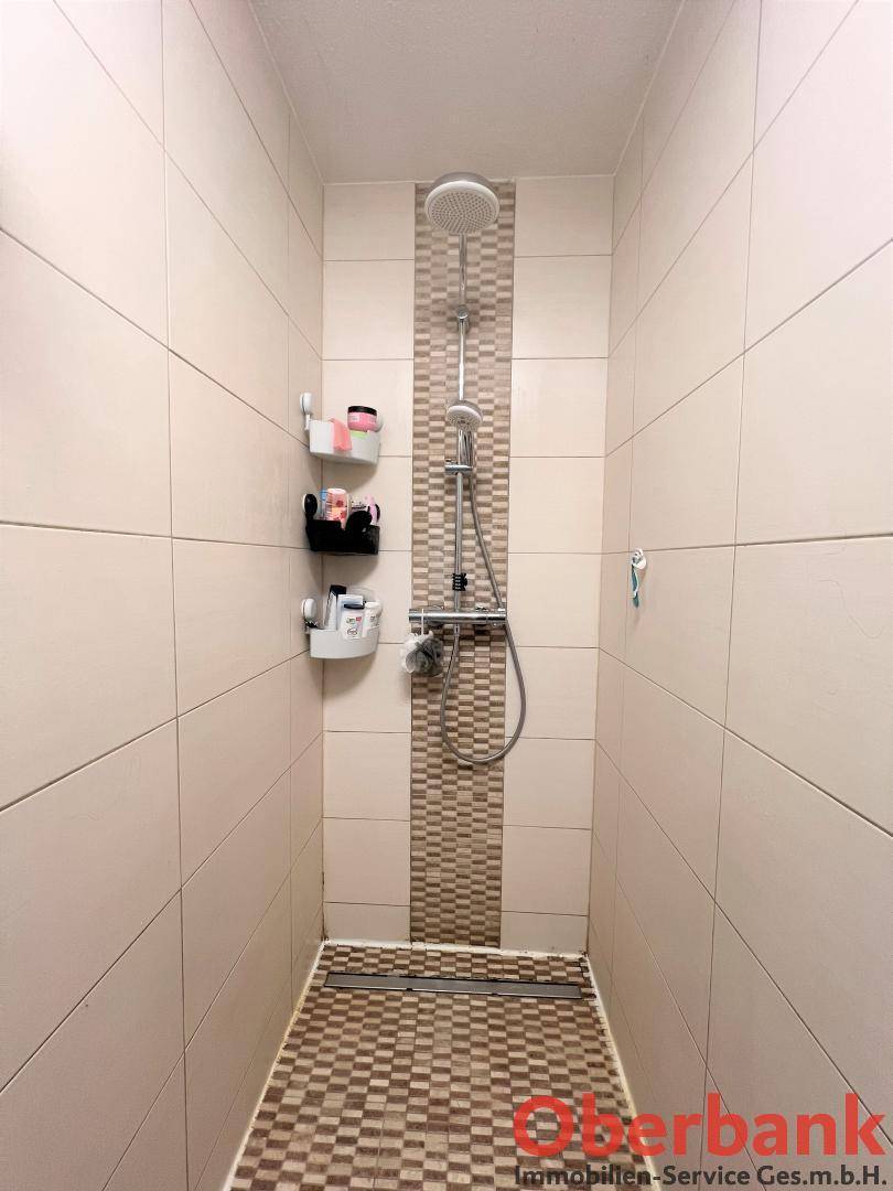 Moderne Duschkabine mit Regendusche und beigefarbenen Fliesen, sauber und funktional.