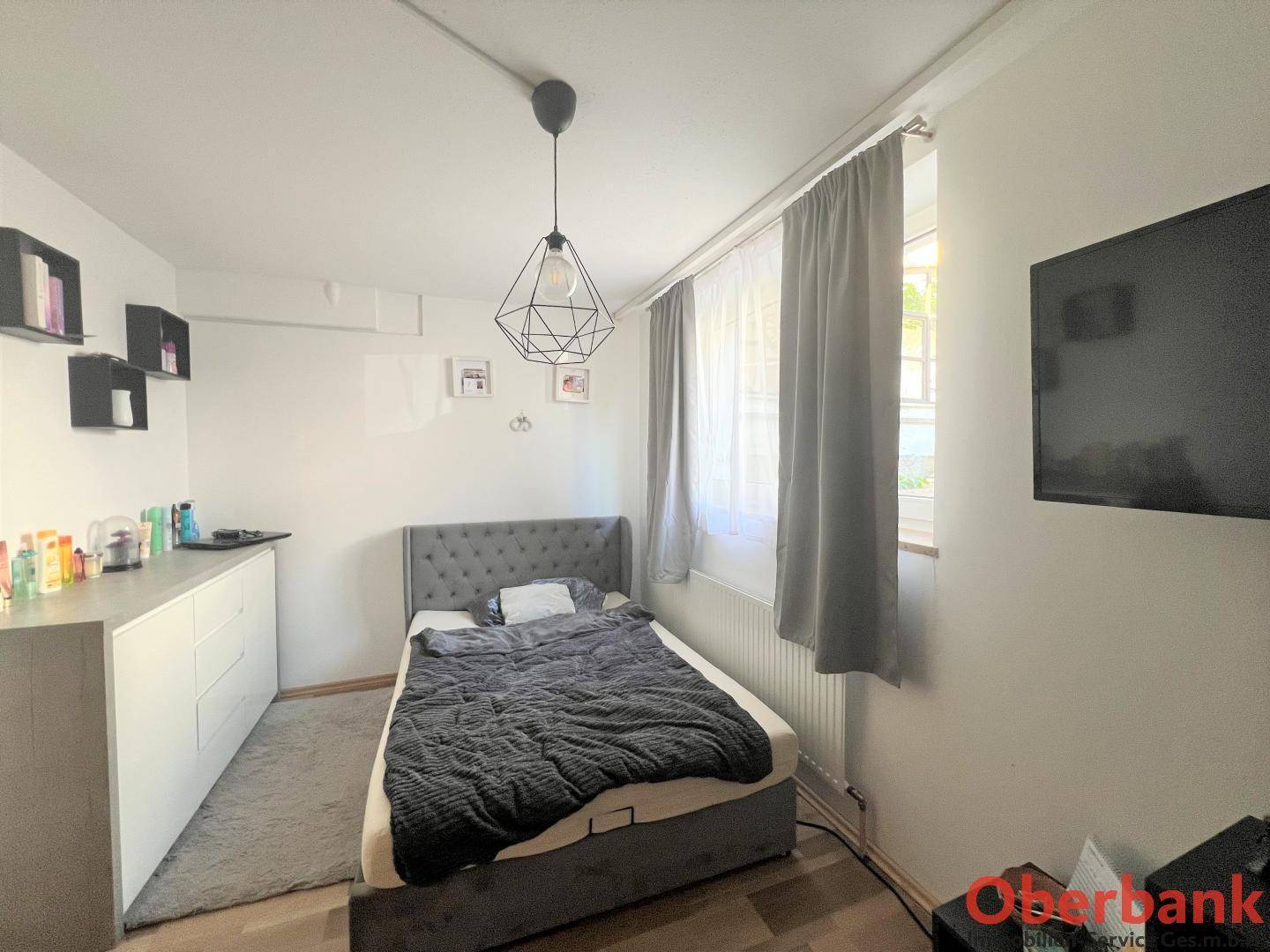 Helles Schlafzimmer mit modernem Bett, Holzboden und Fenster mit Vorhängen.
