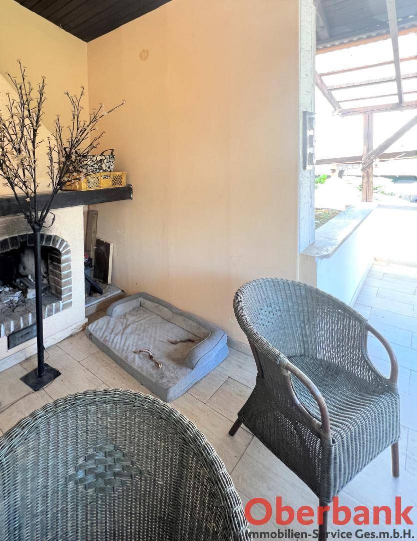 Überdachte Terrasse mit Außenkamin und Rattanmöbeln, perfekt für kühle Abende.