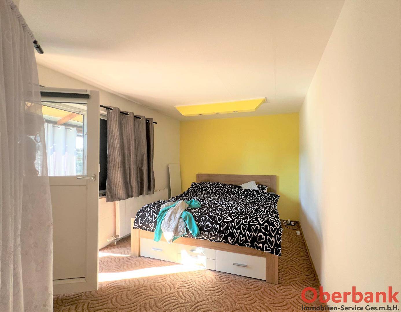 Schlafzimmer mit Doppelbett, gelber Akzentwand und Zugang zu einem Außenbereich.