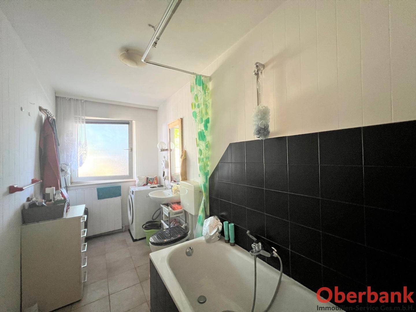 Badezimmer mit Badewanne, WC, Waschbecken, Waschmaschine und einem Fenster für Tageslicht.