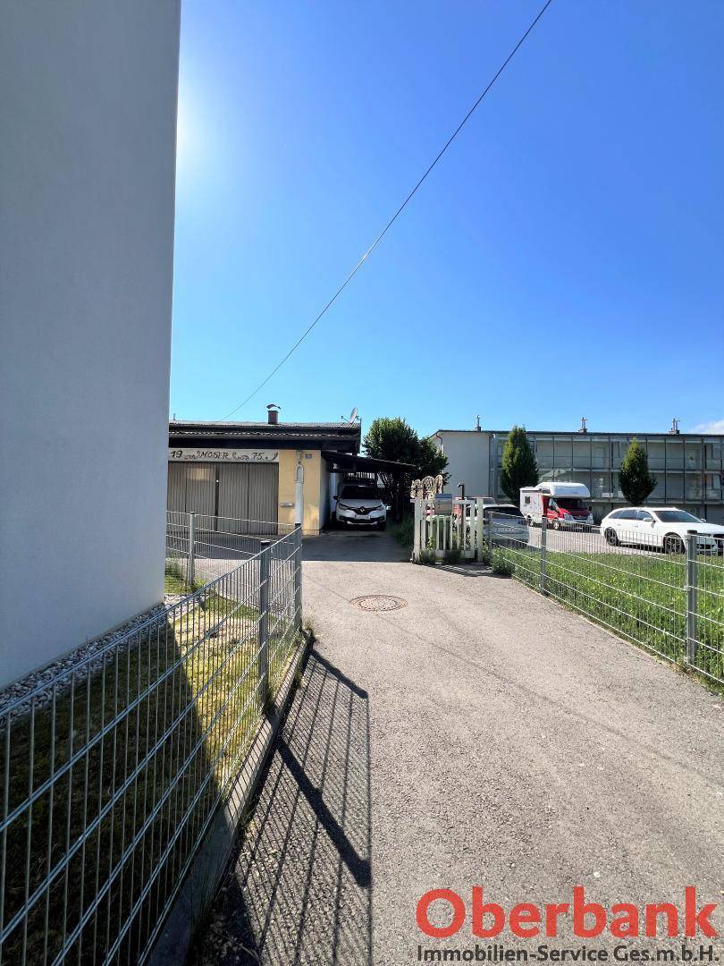 Zufahrtsweg mit Gebäuden auf beiden Seiten und Blick auf die Umgebung an einem sonnigen Tag.