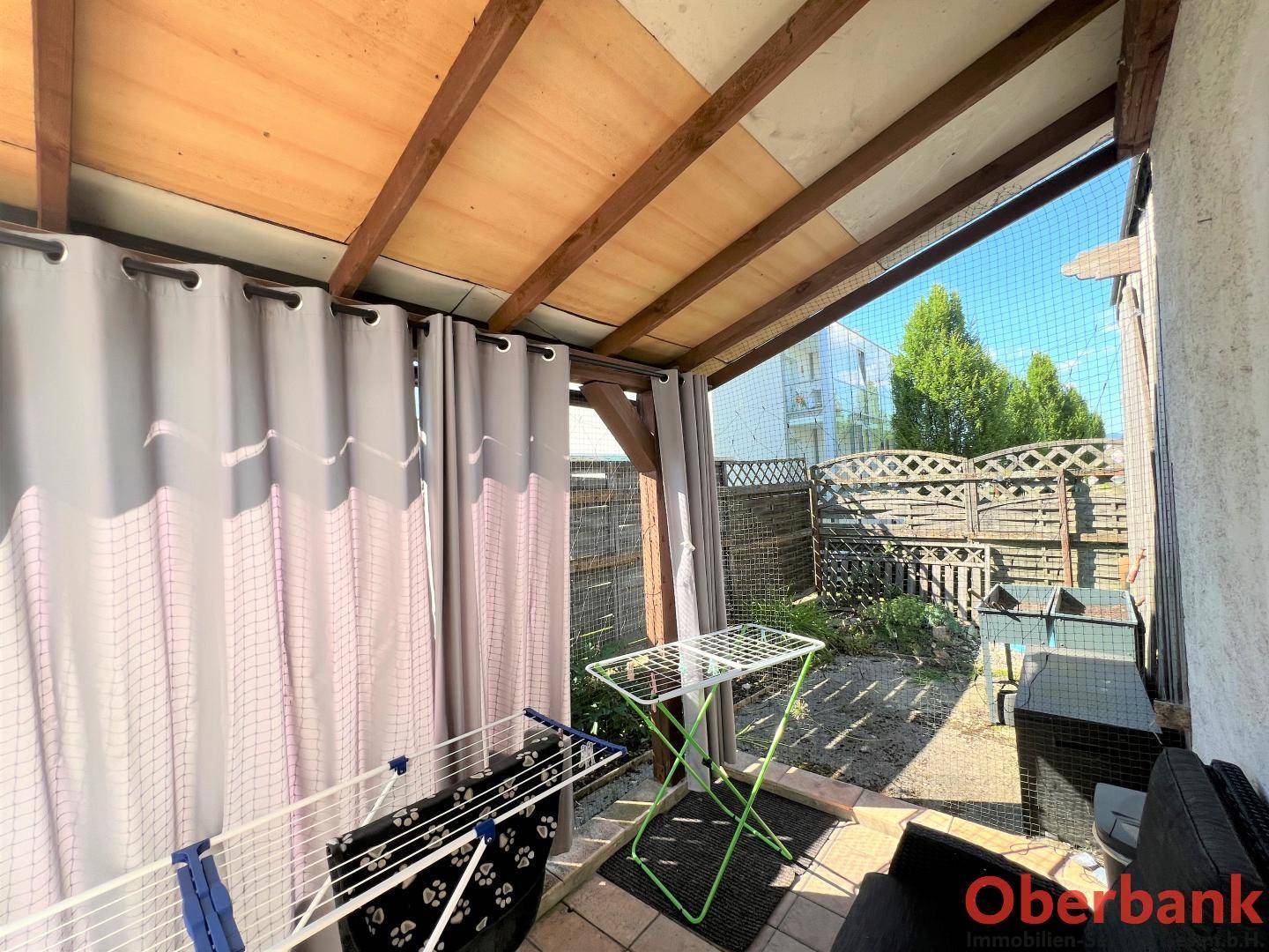 Überdachter Außenbereich, möglicherweise eine Loggia, mit Wäscheständern und Blick in den Garten.