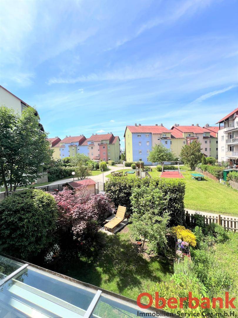 Blick auf den gepflegten Gemeinschaftsgarten mit Liegestuhl und Kinderspielplatz an einem sonnigen Tag.