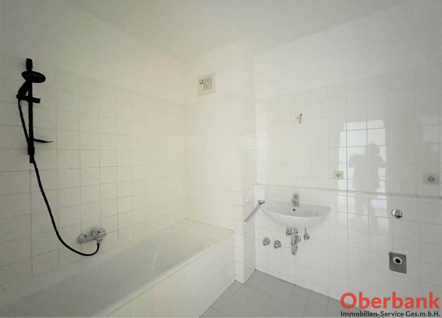 Funktionales Badezimmer mit Badewanne, Waschbecken und weißen Fliesen, schlicht gehalten.