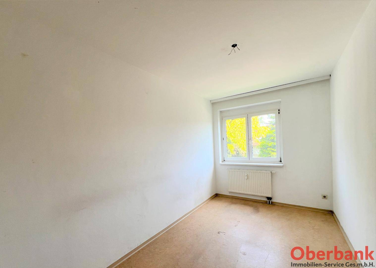 Unmöbliertes Schlafzimmer mit Laminatboden und einem Fenster, das viel Tageslicht hereinlässt.
