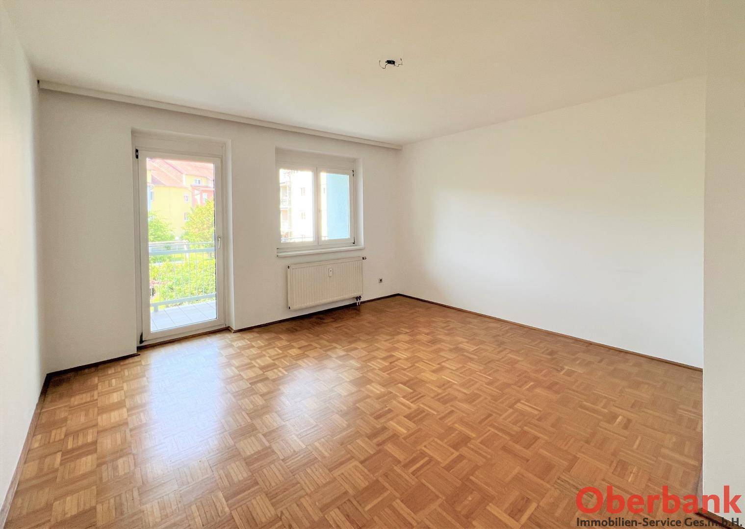 Heller Wohnraum mit klassischem Parkettboden und Zugang zu einem Balkon, unmöbliert.