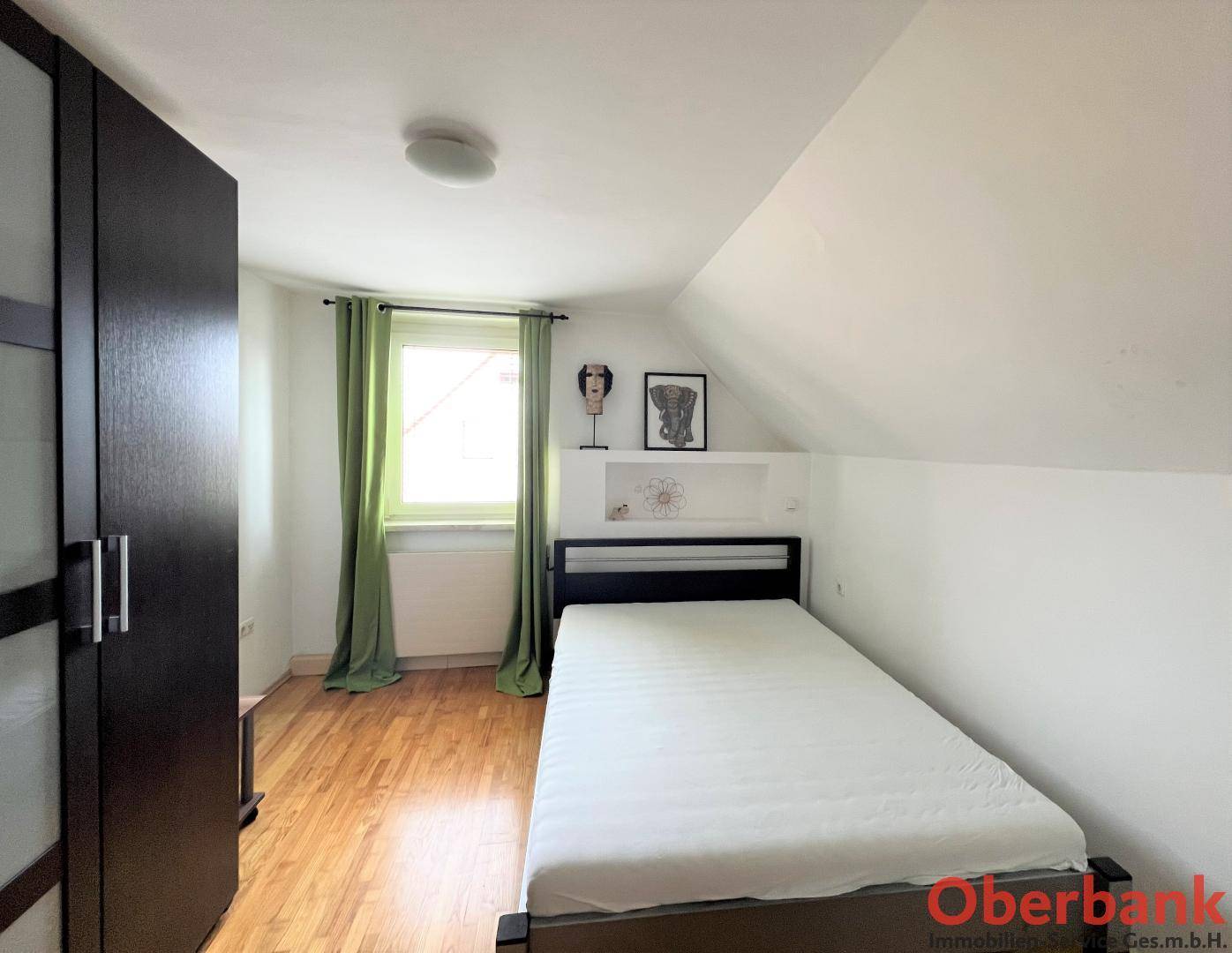 Schlafzimmer im Dachgeschoss mit Einzelbett, Kleiderschrank und grünen Vorhängen.