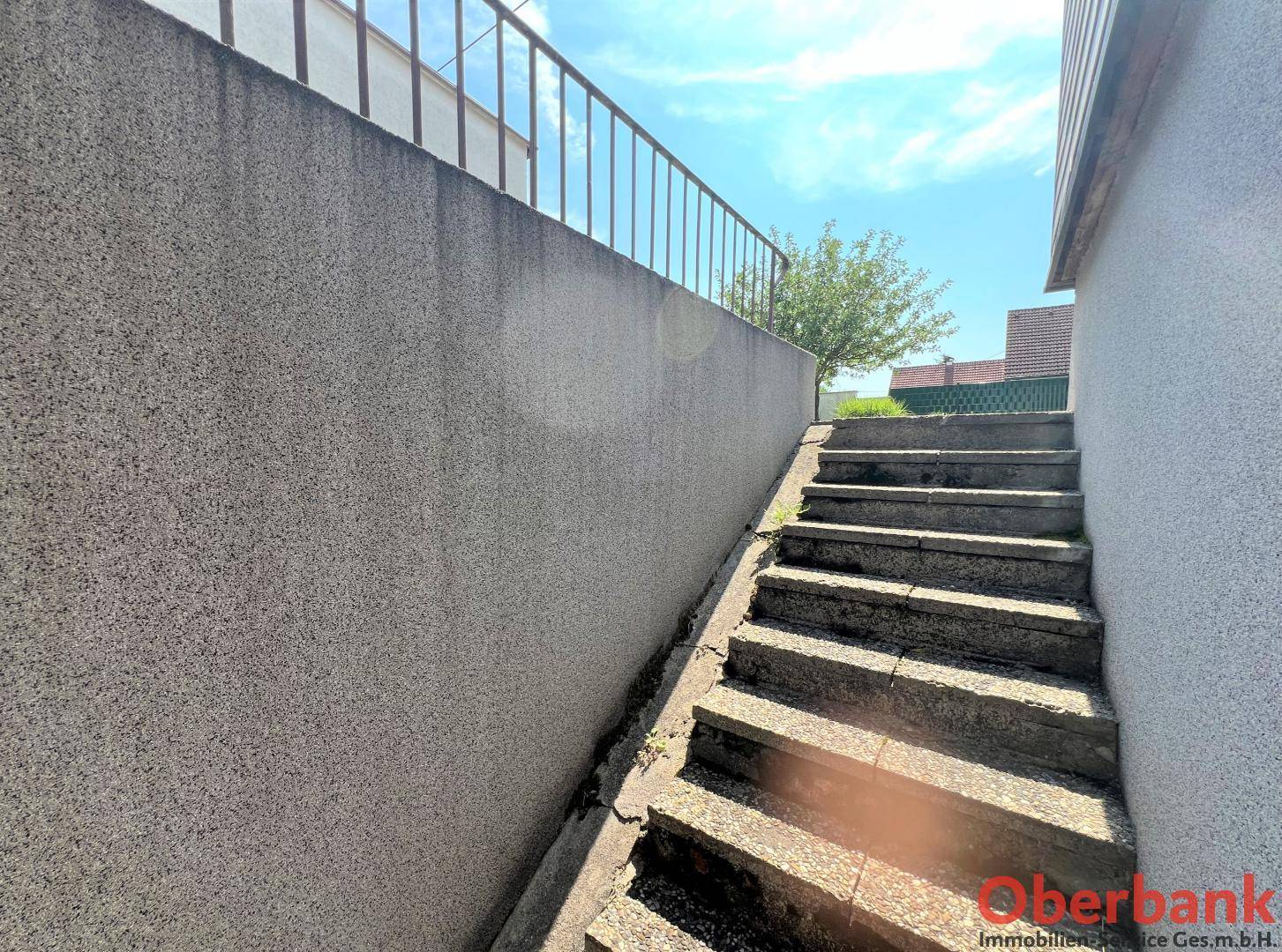 Außentreppe mit Betonstufen und Metallgeländer, die zu einem unteren Bereich des Hauses führt.