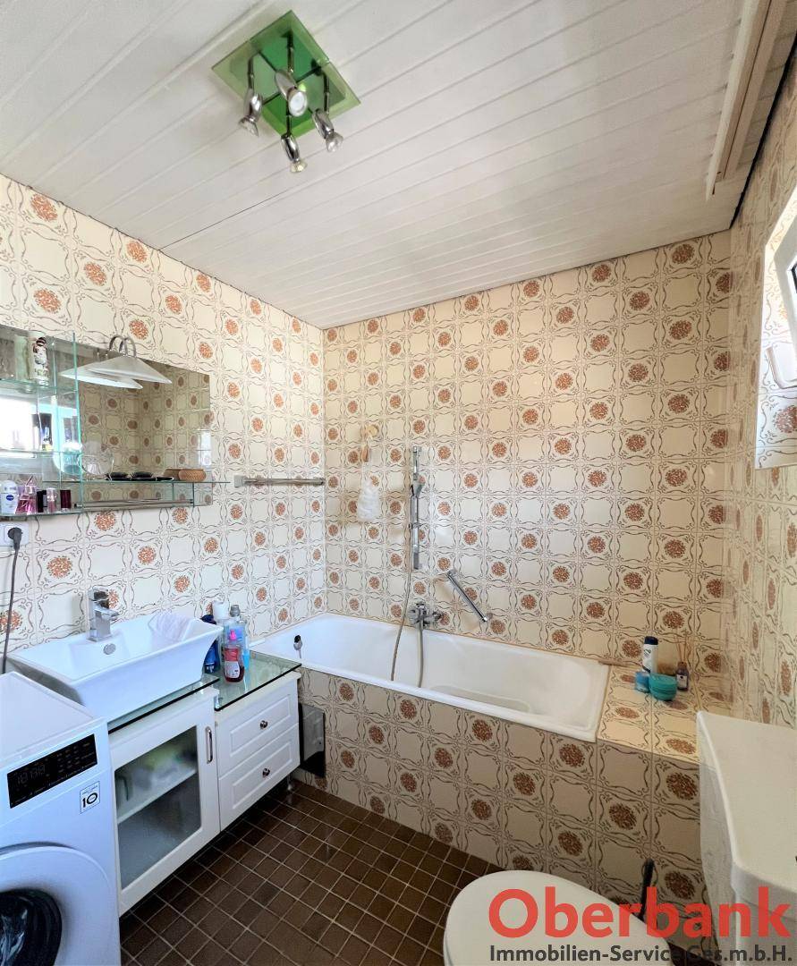 Badezimmer mit gemusterten Fliesen, Badewanne, Waschbecken und Waschmaschine.