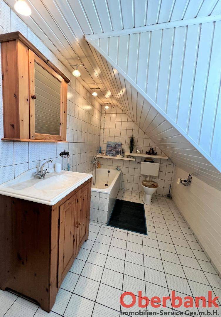 Badezimmer im Dachgeschoss mit Badewanne, Waschbecken und Holzdeckenverkleidung.