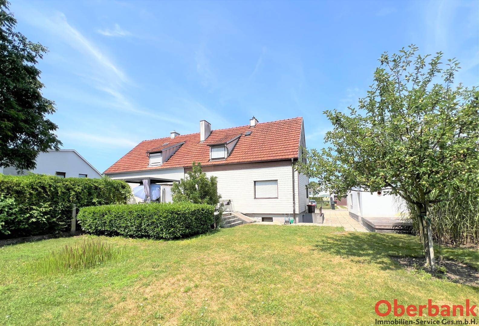 Rückansicht des Hauses mit Garten, Rasenfläche und einer gepflegten Hecke unter blauem Himmel.