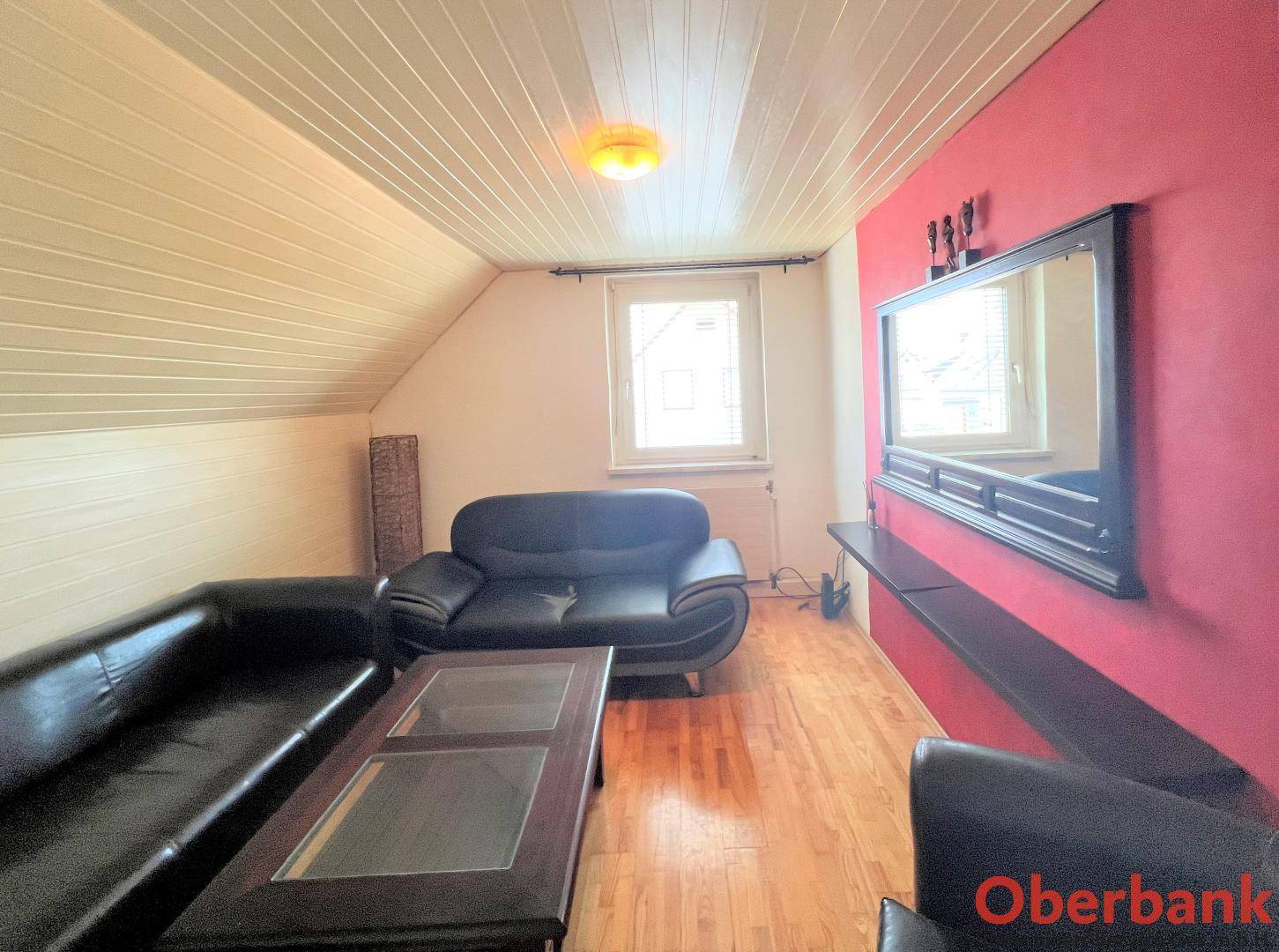 Gemütliches Wohnzimmer im Dachgeschoss mit Schrägen, Ledersofas und roter Akzentwand.