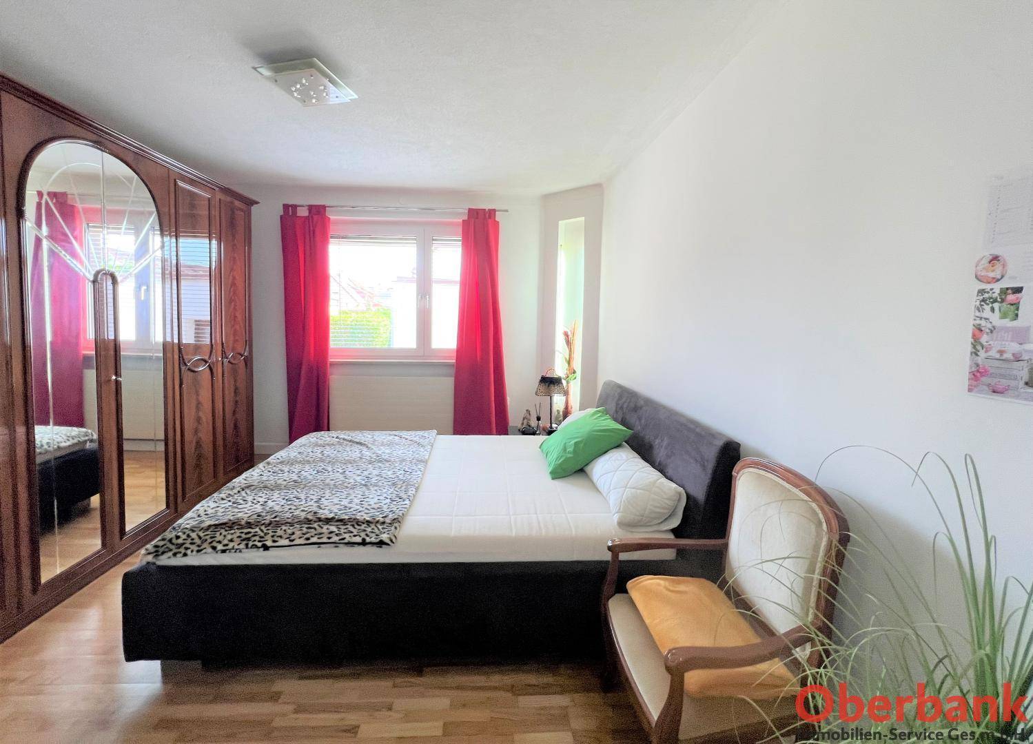 Geräumiges Schlafzimmer mit Doppelbett, großem Holzschrank und roten Vorhängen.