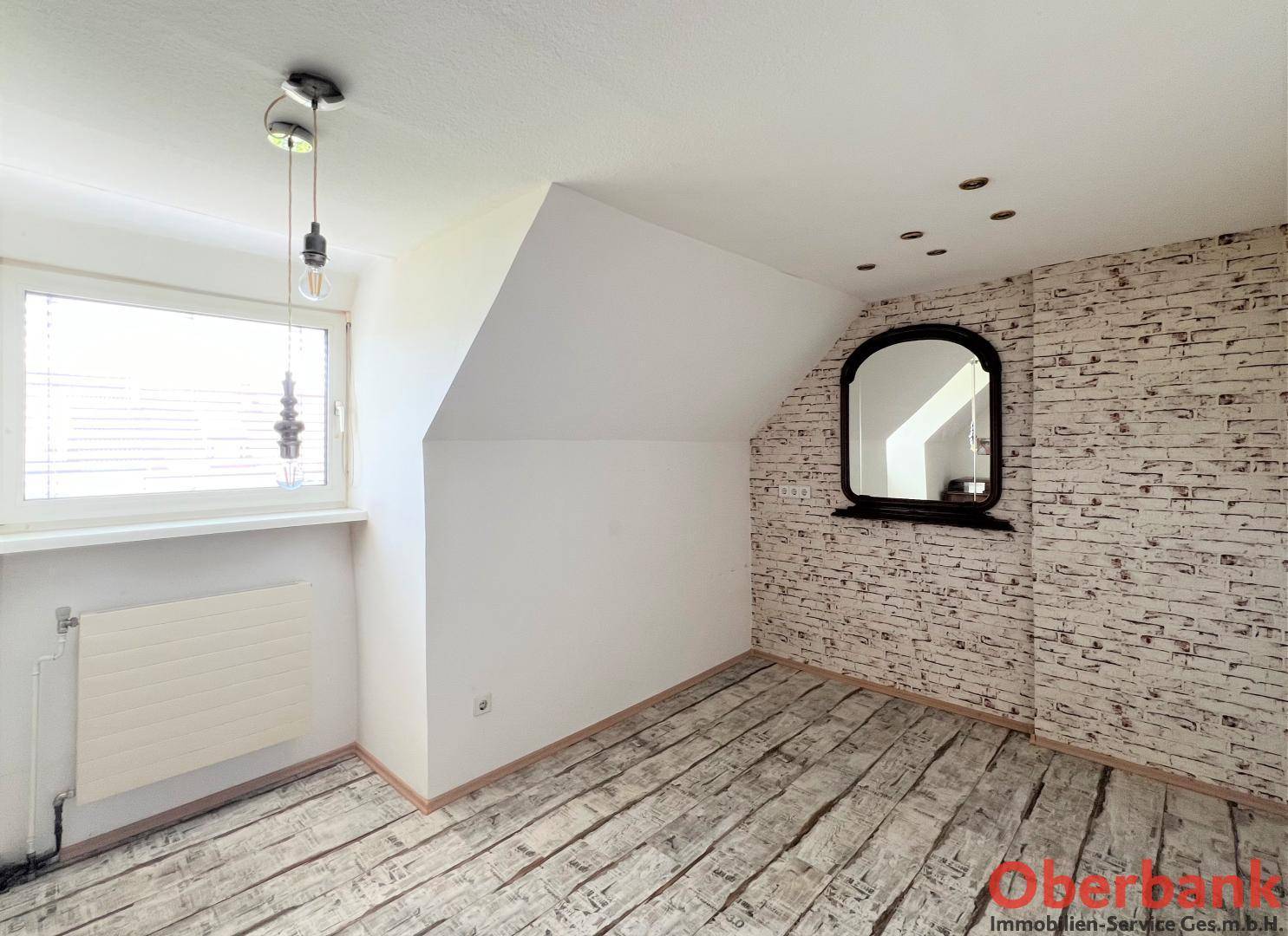 Helles Zimmer im Dachgeschoss mit Schrägen, Fenster und Ziegelmuster-Tapete.