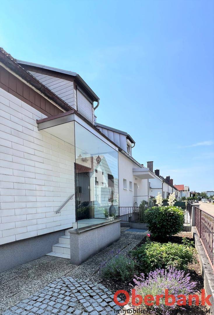 Moderner Hauseingang mit Glasanbau, weißer Fassade und gepflegter Vorgartenbepflanzung.