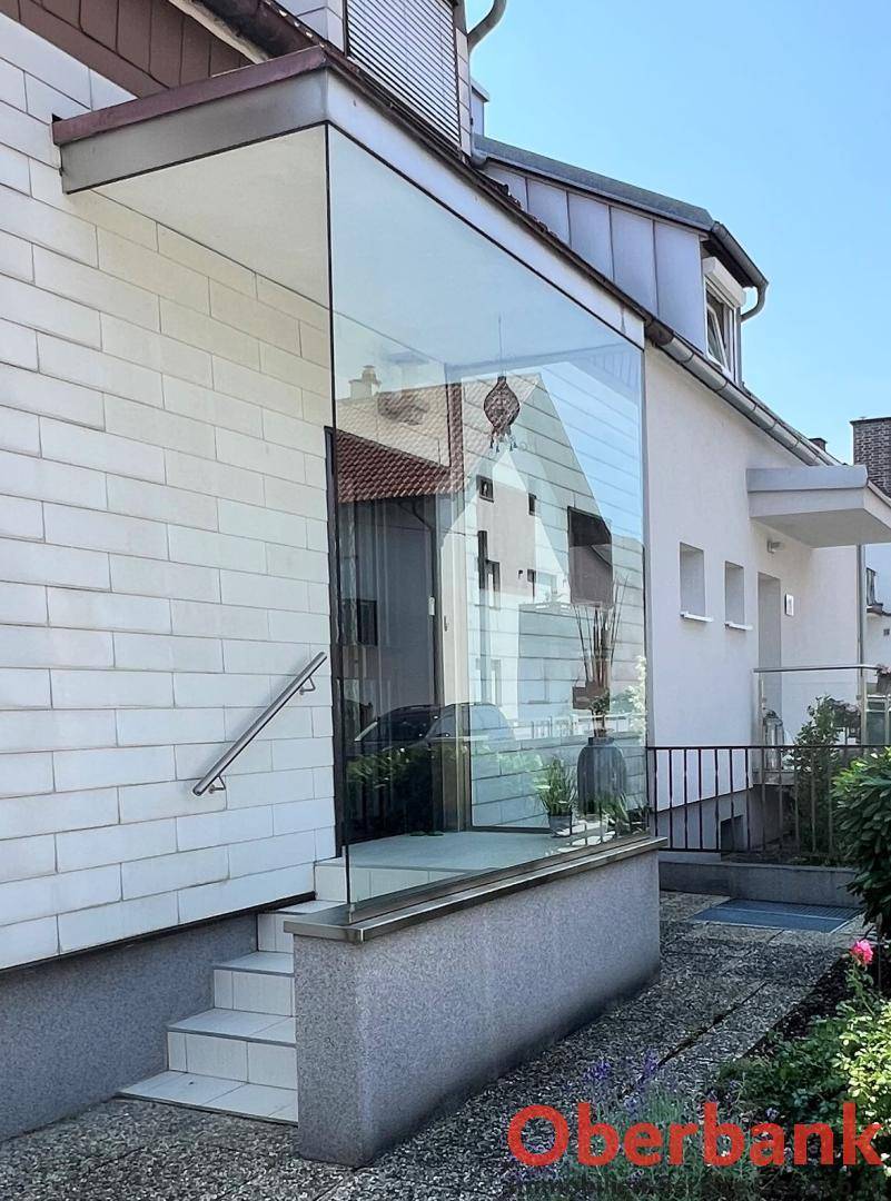 Detaillierte Ansicht des gläsernen Eingangsbereichs mit Treppe und modernem Geländer.
