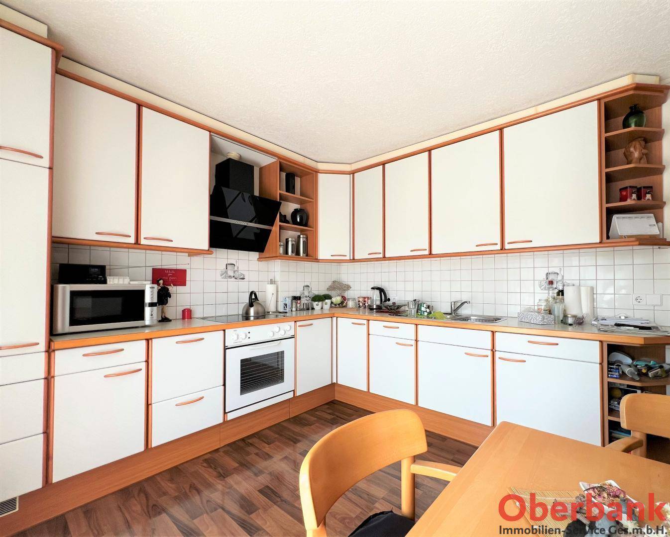 Voll ausgestattete Küche mit weißen Schränken, Holzdetails und integrierten Geräten.