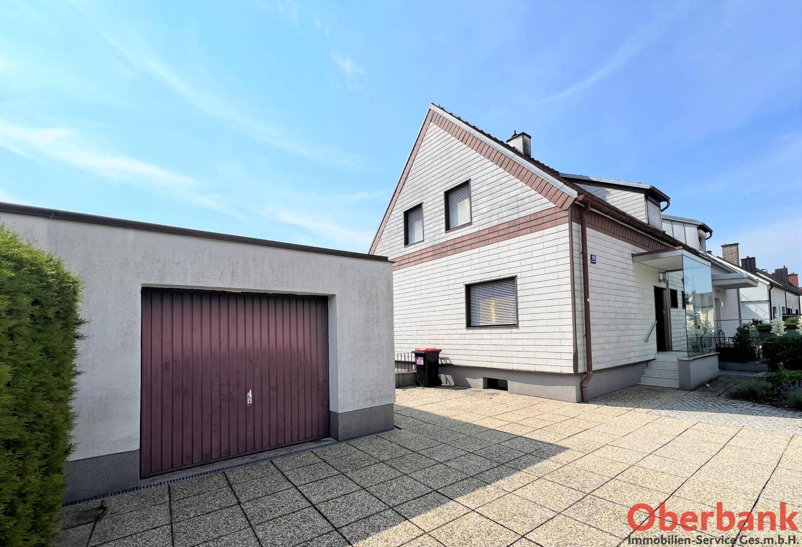 Vorderansicht des Hauses mit Garage, gepflasterter Einfahrt und weißer Fassade unter blauem Himmel.