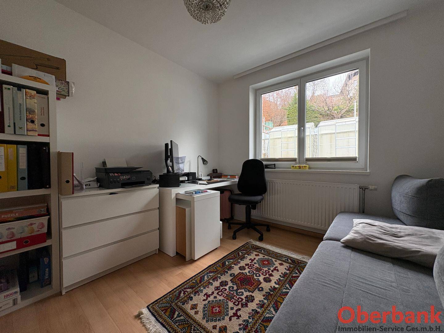 Helles Arbeitszimmer mit Schreibtisch, Regal und Fensterblick ins Freie.