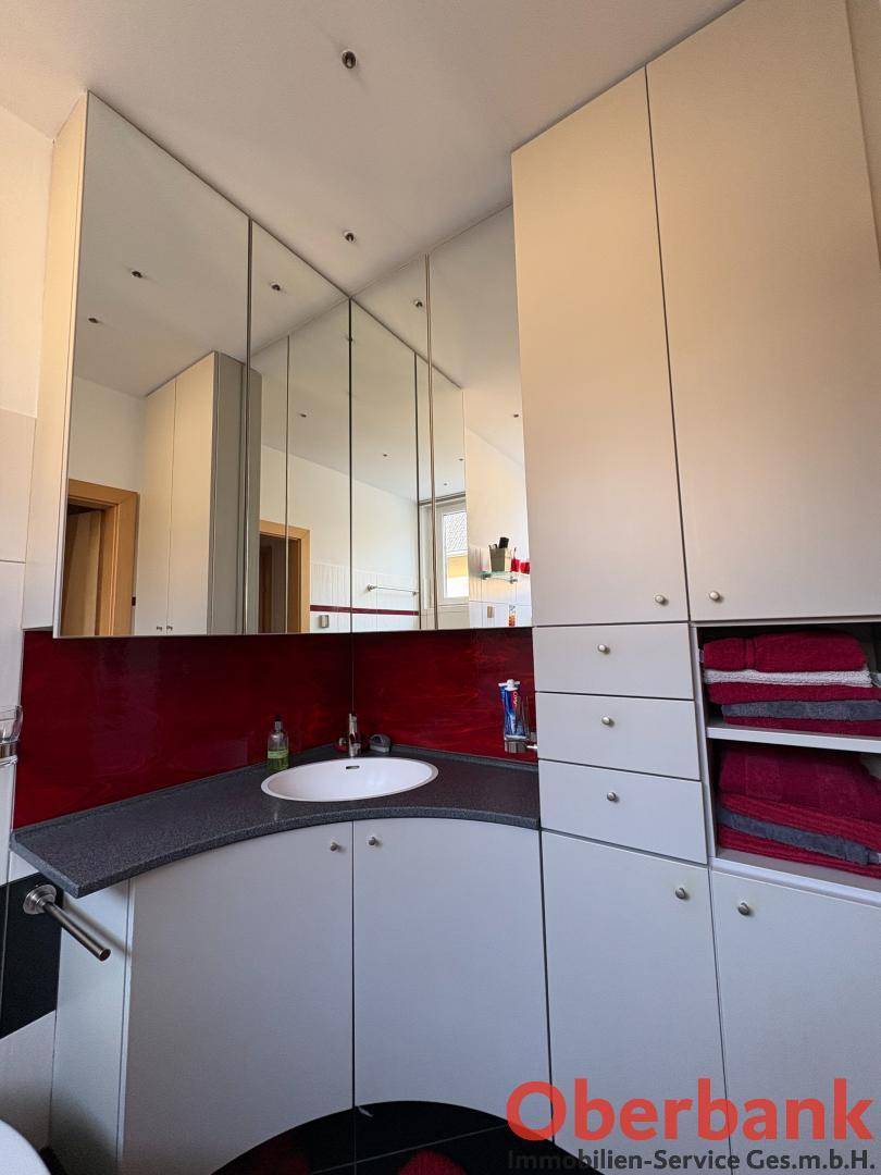 Modernes Badezimmer mit Einzelwaschbecken, Spiegelschrank und roten Akzenten.