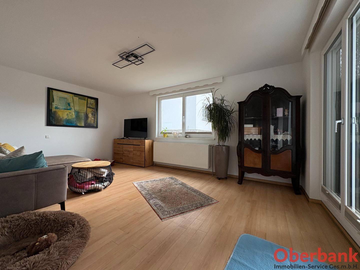 Geräumiges Wohnzimmer mit Holzboden, Sofa und großem Fenster mit Blick ins Grüne.