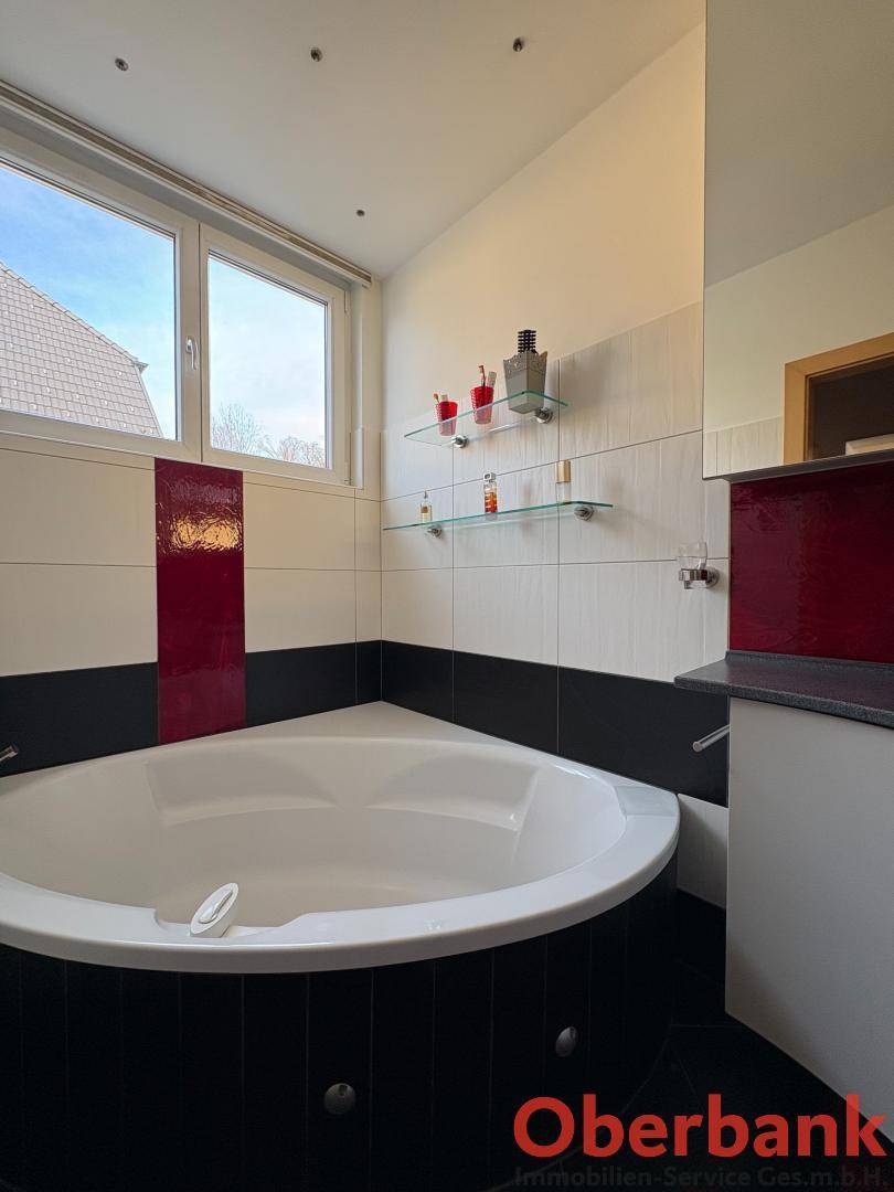 Modernes Badezimmer mit Eckbadewanne, Fenster und farbigen Akzenten.