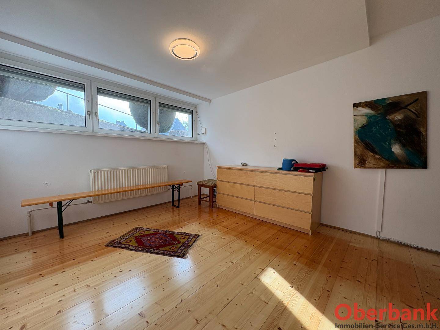 Geräumiges Zimmer mit Holzboden und breitem Fenster, vielseitig nutzbar.