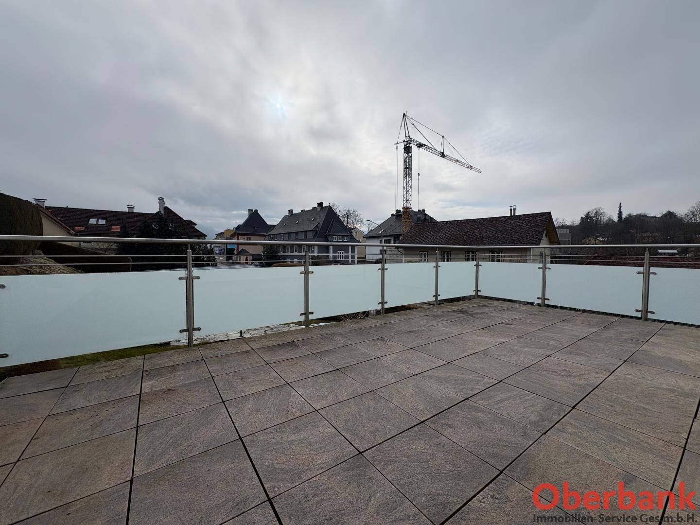 Große Dachterrasse mit Fliesenboden und moderner Glasbrüstung, bietet weite Aussicht.