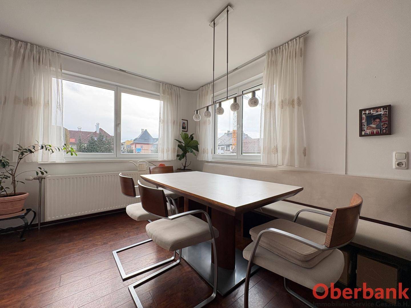 Gemütlicher Essbereich mit Holztisch, Stühlen und großen Fenstern mit Vorhängen.